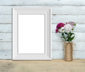 Vertical A4 Vintage White Wooden Frame mockup near a bouquet of sweet-william  stands on a wooden table on a painted white wooden background. Rustic style, simple beauty. 3d render.