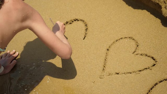 Girl drawing heart symbol on sand beach.