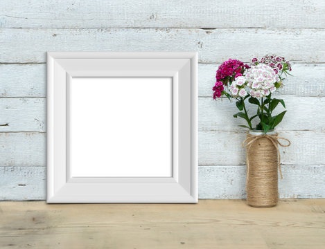 Square Vintage White Wooden Frame mockup near a bouquet of sweet-william  stands on a wooden table on a painted white wooden background. Rustic style, simple beauty. 3d render.