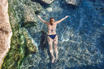 Woman and nature together. Mediterranean leisure and relaxation summer on beach, girl swimming in water. Antique Thermal pool with fragments of ancient columns, Cleopatra's Bath in Pamukkale,Turkey