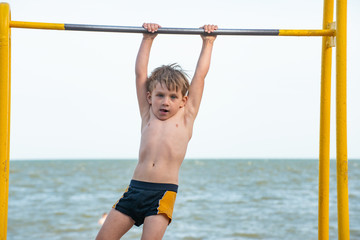 Fototapeta premium The boy on the bar performs the exercises, a strong and muscular athlete.
