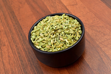 fennel seeds in black bowl on old wooden background.