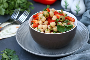 Healthy salad of chickpea, green olives, pepper and parsley, is located on a dark background