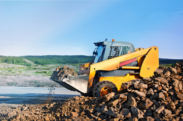 Loader dumping stone on road on the natural background In the countryside.