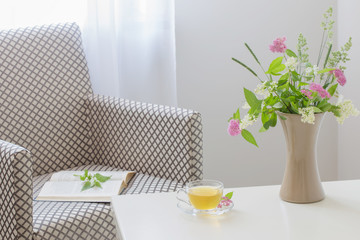 Fototapeta na wymiar cup of tea, open book and summer bouquet in vase indoor