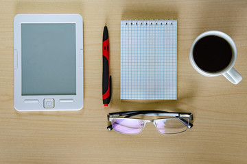 Office table. Tablet, glasses, notebook and pen cup of coffee. Wooden table. Top view