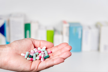 Hand full of pills and capsules with medidice packs in background