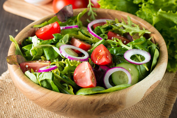 Fresh healthy vegetable salad made of cherry tomato, ruccola, arugula, feta, olives, cucumbers, onion and spices. Greek, Caesar salad in a bowl on wooden background. Healthy organic food concept.