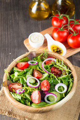 Fresh healthy vegetable salad made of cherry tomato, ruccola, arugula, feta, olives, cucumbers, onion and spices. Greek, Caesar salad in a bowl on wooden background. Healthy organic food concept.