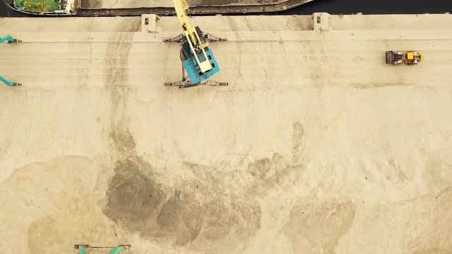 A crane loads sand onto a barge in port. Aerial view. Delivery of industrial cargo and construction materials by water. Extraction of river sand