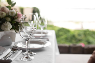 Wedding table setting decorated with fresh flowers in a brass vase. Wedding floristry. Banquet table for guests outdoors with a view of green nature. Bouquet with roses, eustoma and eucalyptus leaves
