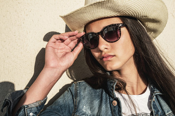 Fototapeta premium young pretty girl posing against background of wall in large hat with brim, jute and sunglasses.