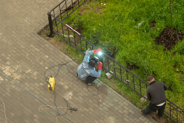 Two men working by welding build a metal fence