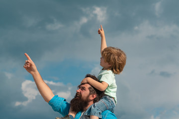 Fathers day. Cute boy with dad playing outdoor. Happy child pointing on summer sky background.