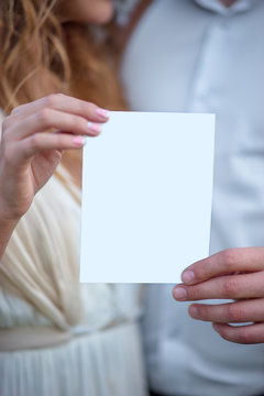 Bride And Groom Holding In Hands White Blank Invitation Card. Male And Female Showing White Card.