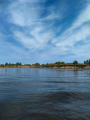 Landscape - in the distance shore, bright sky and clouds reflected in the river