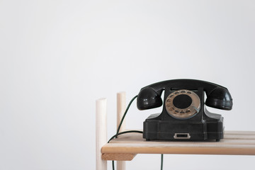 Black old phone on a wooden shelf on white wall background with copy space. Contact us.