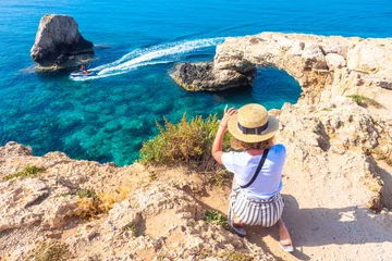 Foto auf Acrylglas Zypern Zypern. Touristen an der Liebesbrücke. Das Mädchen fotografiert die Brücke der Liebe von oben. Die Klippen im Meerwasser. Das Kap Greco. Ayia napa. Das Reiten eines Wasserscooters im Mittelmeer.