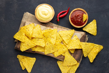 Mexican corn chips nachos with sauces on dark background. Top view.