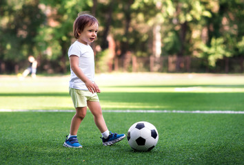 Little football player: toddler boy in sports uniform playing footbal at soccer field in summer day...