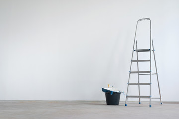 Ladder and bucket with paint roller on a white wall background with copy space. Under construction concept background.
