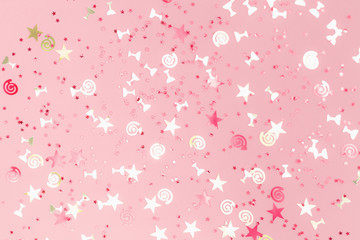 Golden stars flutes and swirls glitter and assorted sparkling confetti partially blurred on trendy pink background. Festive holiday pastel backdrop.