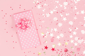 Golden stars flutes and swirls glitter and assorted partially blurred sparkling confetti on trendy pink background with a pink polka dot gift envelope. Festive holiday pastel backdrop.