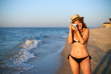 Young authentic woman with vintage retro film camera enjoying tropical beach on summer vacation. Female travel photographer in straw hat taking photos having fun at sea. Real girl unretouched shape. - Powered by Adobe