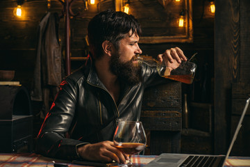 Fototapeta na wymiar The biker coming to the bar. Frustrated man with a beard is drinking from a bottle of whiskey. Problems in relationships. Alcoholism, alcohol addiction and people concept.