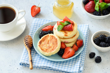 Syrniki, cottage cheese fritters served with fresh berries, honey and cup of coffee