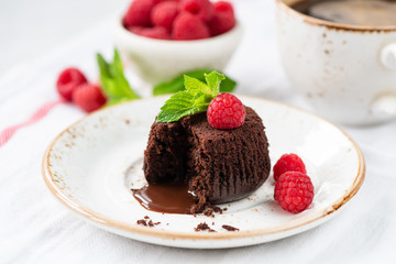 Warm Chocolate Lava Cake with Bite Taken Out of Molten Center and Raspberries on White Dessert Plate. Closeup View