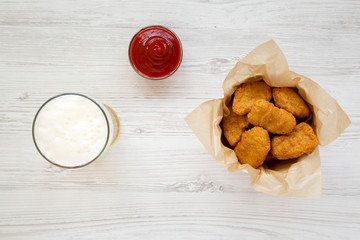 Chicken nuggets in a paper box, ketchup and glass of cold beer on a white wooden surface. Overhead, from above, flat lay.