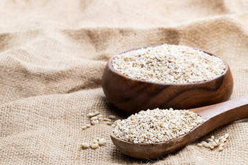 Barley groats in wooden bowl on burlap background