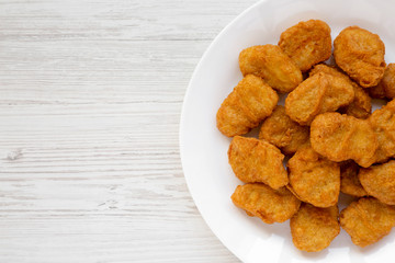 Chicken nuggets on a plate on a white wooden surface, top view. Overhead, from above, flat lay. Copy space.