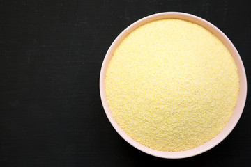 Dry semolina durum flour in a pink bowl over black background, top view. Overhead, from above, flat lay. Copy space.
