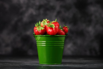 Strawberries in a bucket on the dark concrete background