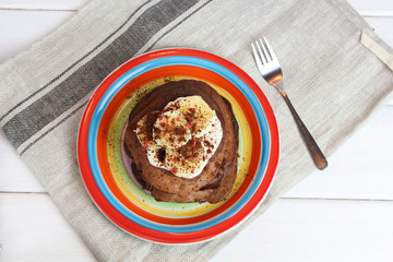 gluten-free chocolate pancakes, proper diet vegetarian food for breakfast with cocoa, Greek yogurt and banana on colorful rainbow colored plate of LGBT flag colors, top view. LGBT breakfast concept