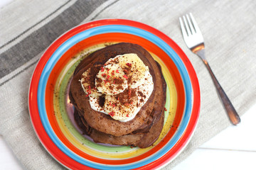 gluten-free chocolate pancakes, proper diet vegetarian food for breakfast with cocoa, Greek yogurt and banana on colorful rainbow colored plate of LGBT flag colors, top view. LGBT breakfast concept