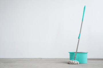 Bucket with a mop on a floor on a white wall background with copy space. Wet cleaning concept background. - obrazy, fototapety, plakaty