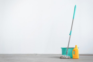 Bucket with a mop and bottle of detergent on a floor on a white wall background with copy space....