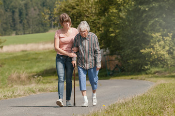 Young woman helps senior woman walking with stick - 273537588