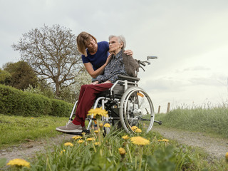 Young woman comforts old sad woman in wheelchair - 273537592