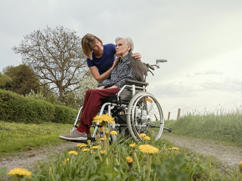 Young woman comforts old sad woman in wheelchair