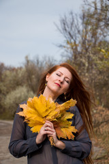 Portrait of young redhead woman with bouquet of yellow leaves