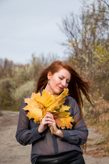 Portrait of young redhead woman with bouquet of yellow leaves