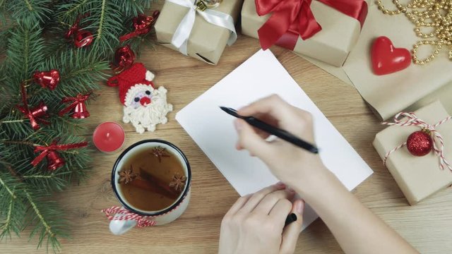 Woman hands writing new year to do list on white paper sheet, planning her future. Christmas decoration with fir branches, gifts. Flat lay. Top view. Mockup, copy space for your text.