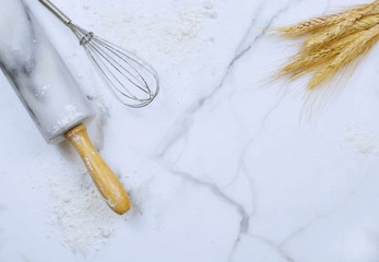 Flat lay on marble table top. Copy space. Food or kitchen themed image of rolling pin, wire wisk, flour and wheat. Copy space.