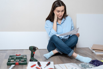Astonished brunette woman with the instructions for Assembly of furniture in the hands of sitting...