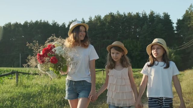Children are three girls with bouquet of flowers holding hands walking along a country road