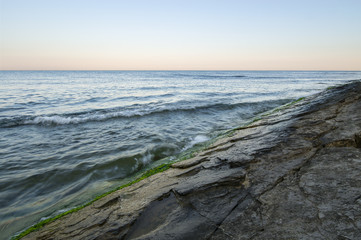 Textured horizontal rock against the sea, the waves turned into fog, early morning.